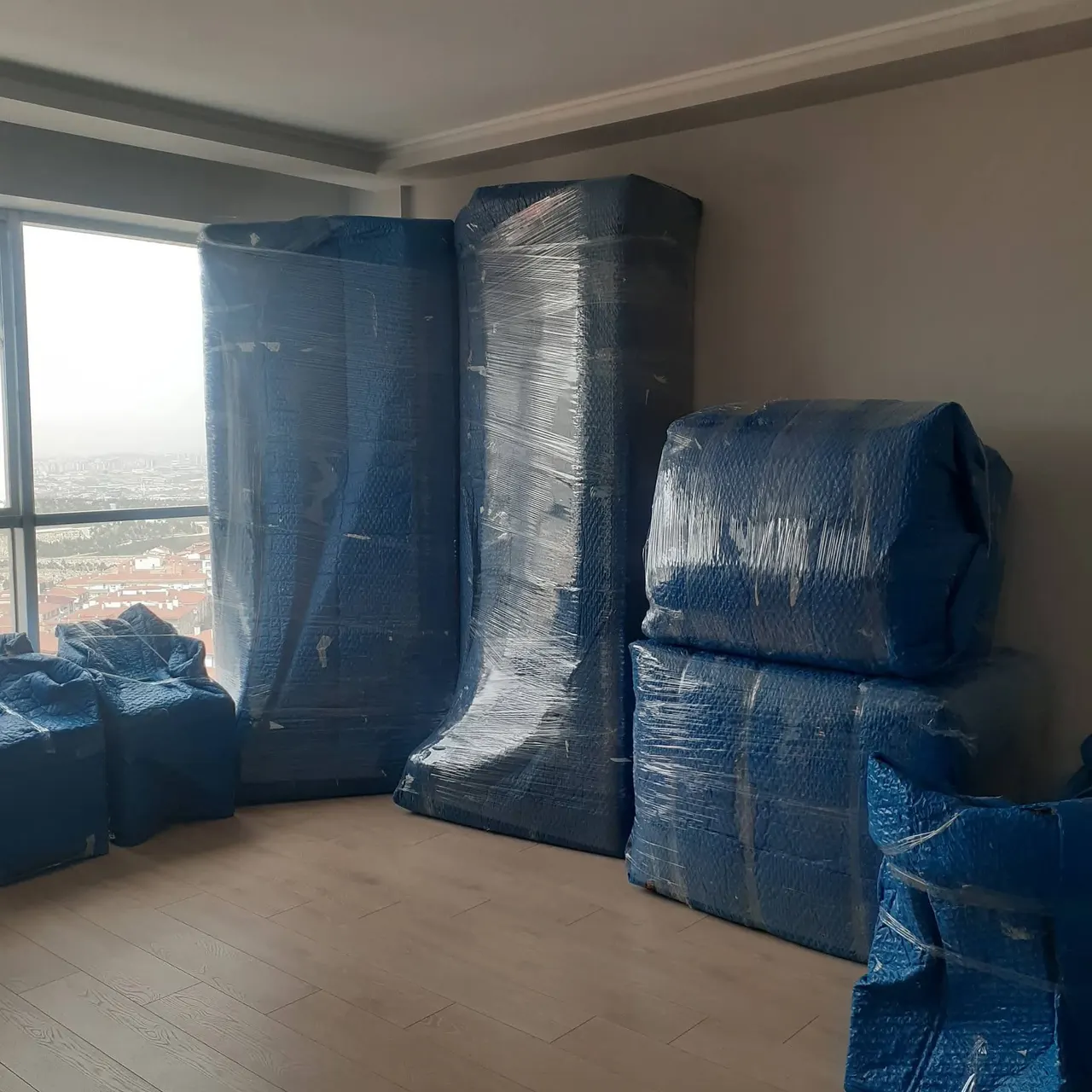 Evden eve nakliyat için taşıma battaniyesi ve streç filmle paketlenmiş dolaplar ve koltuklar boş dairede sıralanmış